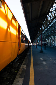Looking along the side of yellow train carriages at a station with converging lines
