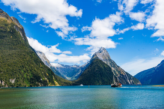 Large motor sail boat on blue water with mountains and blue cloudy sky