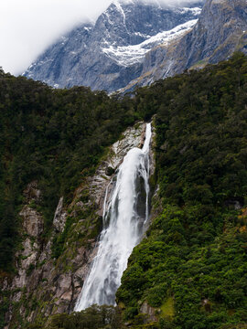 High mountainside waterfall with snow and cloud capped mountains behind