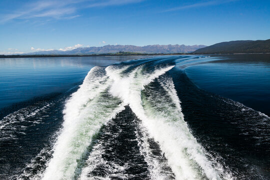 Wake of a boat on a tranquil blue lake with mountains and blue sky