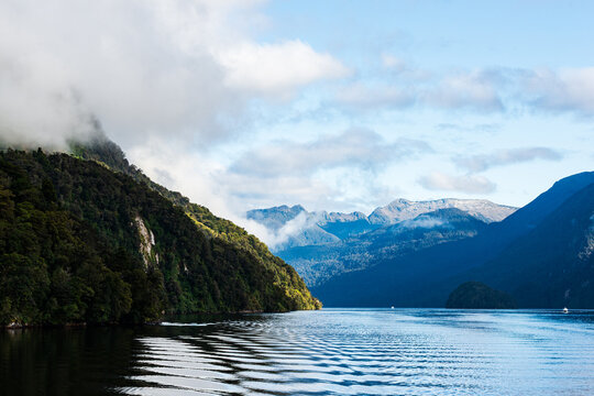 Early morning view of ripples in blue water surrounded by mountains with low clouds