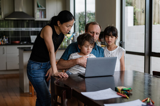 Parents and children gather around a laptop, together in the kitchen