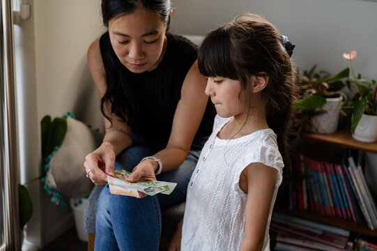 A mother shows different New Zealand banknotes to her young daughter in a living room