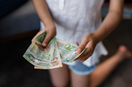 Young child kneeling with a few New Zealand twenty-dollar notes in hand inside a home