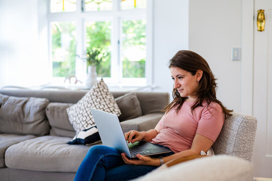 Italian woman sitting on a couch working on her laptop inside home