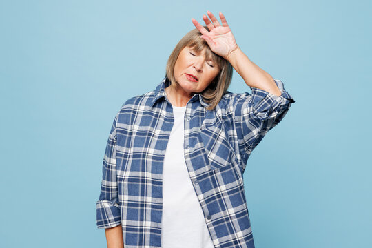 Elderly sad blonde woman 50s years old wear checkered shirt casual clothes put hand on forehead suffer from headache isolated on plain pastel light blue background studio portrait. Lifestyle concept.