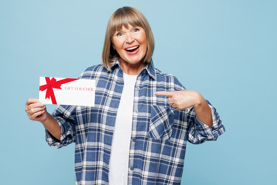 Elderly happy blonde woman 50s years old wear checkered shirt casual clothes hold certificate coupon voucher card for store isolated on plain pastel light blue background studio Lifestyle concept