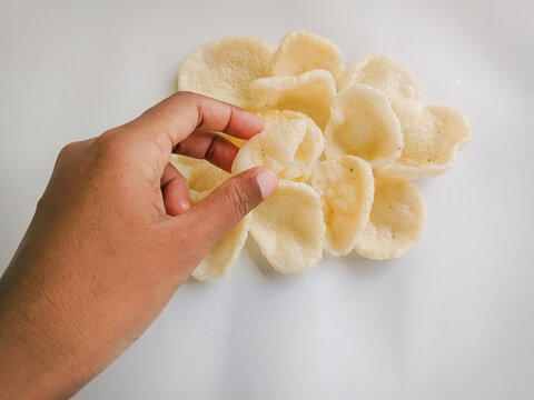 A hand picking up crunchy Indonesian prawn cracker from a pile. Deep fried krupuk udang snack on plain white background