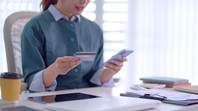Asian businesswoman using credit card mobile phone online shopping ecommerce payment transaction modern office desk workspace professional female entrepreneur