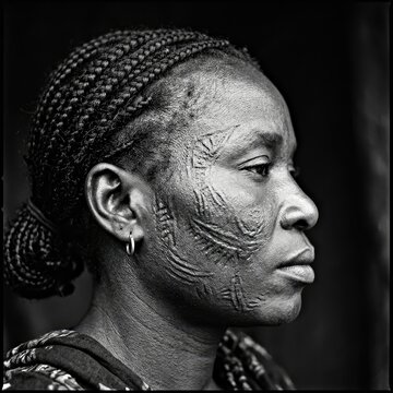 Scarification Markings of Ancestry: A striking black and white portrait of an African woman, her face adorned with intricate scarification marks, telling a story of tradition and heritage.