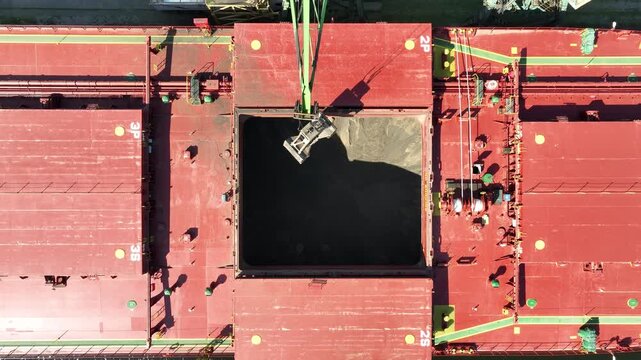 Unloading dry cargo ship of wheat by cranes in port. Aerial view loading into holds of sea cargo vessel