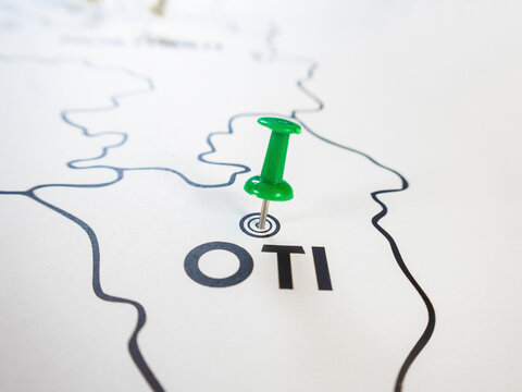 A close-up shot shows a green pushpin marking the "OTI" region on a clean, minimalist black-and-white map of Ghana, highlighting a specific travel destination or geographical point of interest.