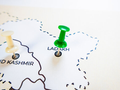 A close-up shot of a white political map of northern India, focusing on Ladakh marked by a green pushpin. A cream-colored pin marks Jammu and Kashmir next to a dashed boundary line.