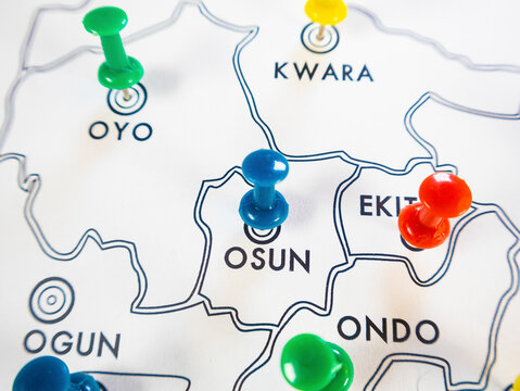 A close up shot of a white Nigerian state map. Brightly colored pushpins blue, red, green, and yellow mark specific southwestern states including Osun, Ekiti, Oyo, and Kwara to pinpoint locations.