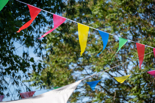 Bunte Wimpelgirlanden h&auml;ngen bei sonnigem Wetter zwischen B&auml;umen im Freien als festliche Dekoration f&uuml;r eine Gartenparty, ein Festival oder eine fr&ouml;hliche Outdoor-Veranstaltung