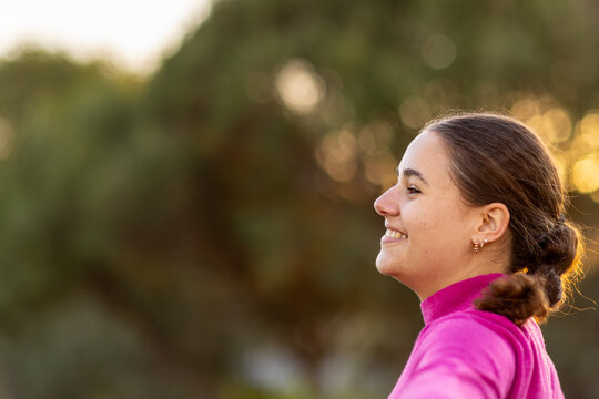 head and shoulders of young woman in profile against blurry dark background of trees
