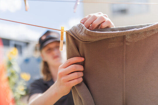 A person's hands secure a garment to a clothesline with a peg