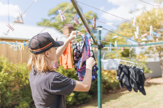 A young person wearing a baseball cap taking washing off the line outdoors