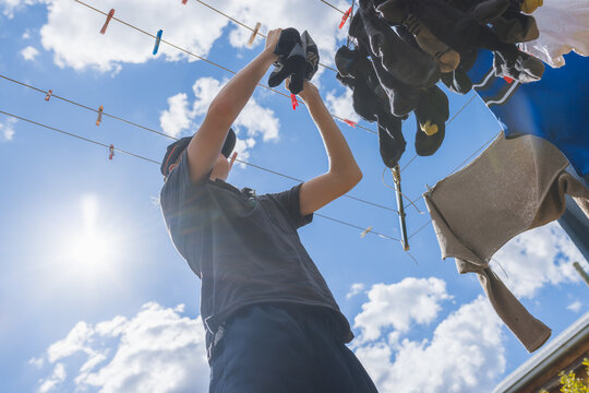 Teen gathering clean washing from clothes line on sunny day, low angle