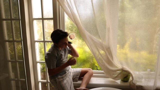 12 year old boy at bathroom window looking out, combing his hair