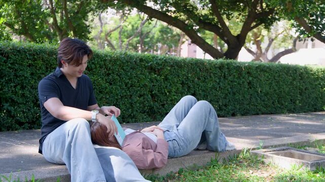 Young Thai University Couple Relaxing and Reading in a Sunny Campus Park