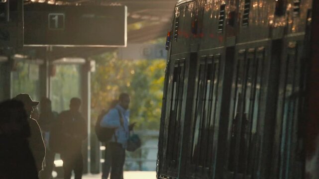 Passengers wait at the subway station as the train approaches in the late afternoon light