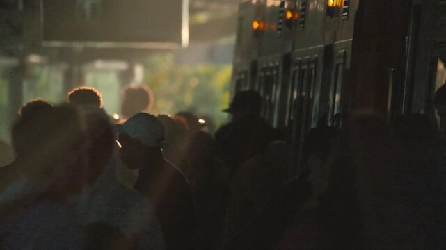 People getting on and off a train at a busy station in the late afternoon light