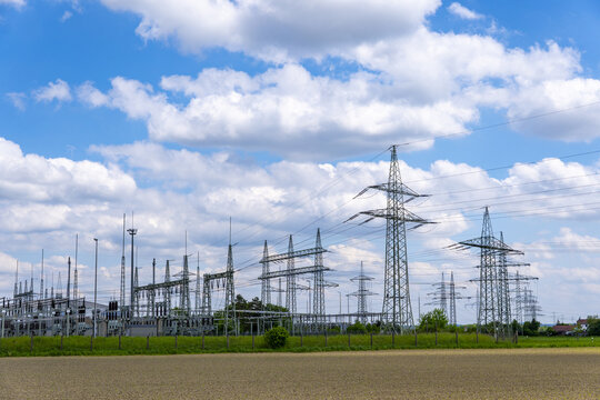 View of Kraftwerk Irsching power plant substation and high-voltage transmission towers standing in a field under a blue sky with clouds in Vohburg an der Donau, Bayern, Germany.