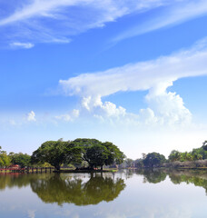 Fototapeta premium Ruins of ancient temple on island, Sukhothai historical park, Thailand. Picturesque landscape with tree and pond, Sukhothai old city, Northern Thailand. Topic of vacation, travel, trip, cruise, tour