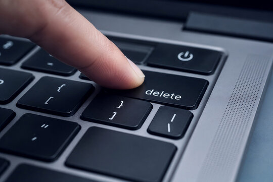 Finger pressing delete key on laptop keyboard for data removal, digital security, editing and technology concept
