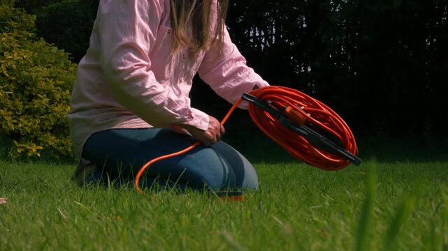Woman rolling long electric cable in garden grass