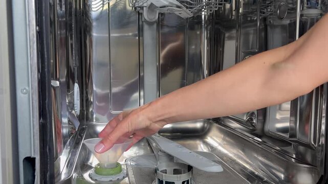 the person pours white granular dishwasher salt from a grey container into the funnel, refilling the reservoir to help soften the water and prevent limescale buildup.