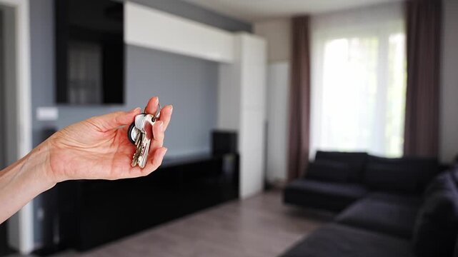 Hand holding apartment keys in furnished resale apartment living room interior. Secondary housing purchase and existing property ownership concept