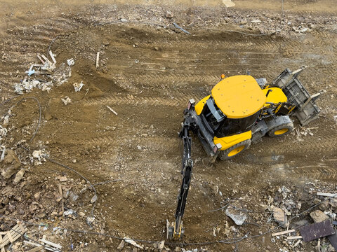 View of a yellow backhoe loader working on a construction site with tire tracks on the brown soil and scattered debris Sariyer, Istanbul, Turkiye.