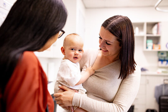 Little boy unsure about medical professional, holding tightly to her mother's shirt