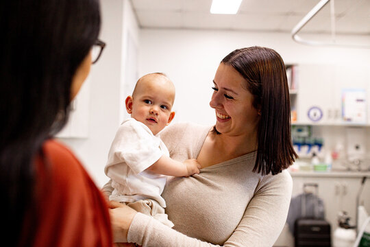 A baby boy unsure about the woman talking to them, his mother laughing at his reaction