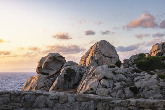 View of the granite rock formations with people standing on the boulders during sunset Capo Testa, Sardegna, Italy.