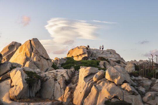 View of the unique granite rock formations of Capo Testa with people standing on the peaks under a soft sunset sky Capo Testa, Sardegna, Italy.