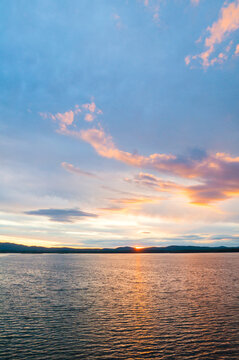 Picturesque summer sunset water landscape, dramatic sky over the rippled water surface and the sun setting behing the mountains