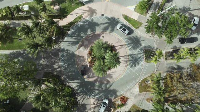 Overhead drone shot of a circular intersection in Key Biscayne, FL, featuring lush palms, brick paving, and vehicles weaving through the island traffic.