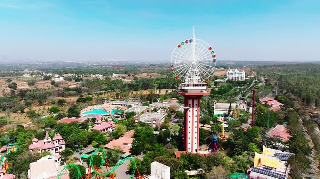 Wonderla amusement park in Bangalore features a large Ferris wheel and tall observation tower surrounded by green rides and pools. Aerial view captures the sprawling park layout against.
