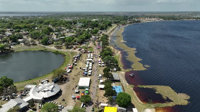 igh-altitude aerial of Pig on the Pond, a beloved Central Florida festival in Clermont, featuring rows of vendors, fair attractions, and a lively crowd by the water.
