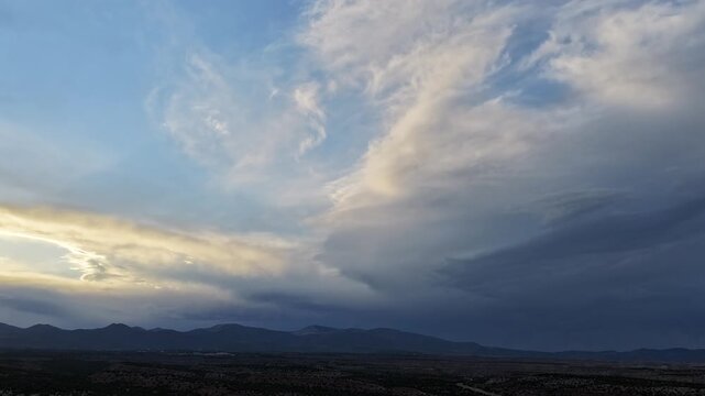 4K surreal drone timelapse captures varied cloud patterns over a vast desert landscape. Cinematic aerial motion reveals a striking beam of sunlight shining through a barrel of dual cloud layers.