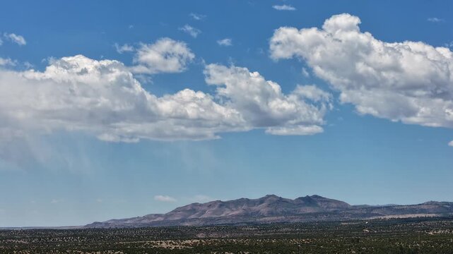 4K steady timelapse captures lightly raining clouds shifting over a rugged southwest mountain. Cinematic atmospheric weather footage reveals gentle precipitation and a moody overcast desert vista.