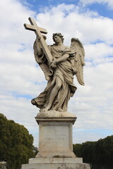 Obraz premium A majestic marble angel statue holding a cross, silhouetted against a bright, cloudy sky in Rome.