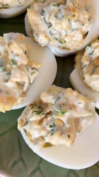 Macro close-up of creamy deviled eggs with herb-speckled filling, styled as a rich homemade appetizer on a serving platter for brunch or holiday entertaining.