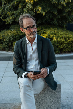 Senior man with glasses thinking while checking phone
