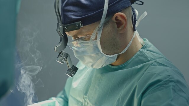 Focused doctor man male surgeon in uniform using electrocautery instrument tool medical equipment cutting burning with smoke doing neurosurgical operation physician practitioner surgery medicine work