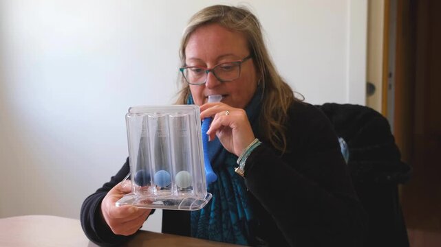 Respiratory therapy woman using spirometer device for lung training and rehabilitation at home.  