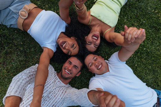 Diverse friends lying on grass holding hands